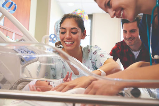 Medical professionals, patient, and family member smiling looking at newborn baby.